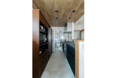 グレーのフロアタイルと天井の木目が調和するキッチン。奥には大容量のパントリーを設置。