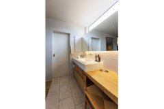 キッチンとつながる造作洗面台。フラットな一面鏡と間接照明でホテルライクな雰囲気を演出。